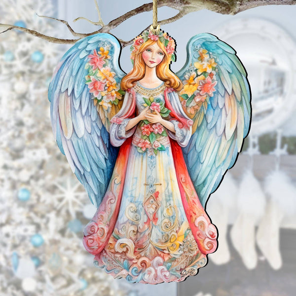 The Ornament: Angel Blue Wings Floral Design Wooden Christmas Tree Ornament by G Debrekht hangs from a branch, featuring vibrant wings and a floral crown, with a white Christmas tree and stockings blurred in the background.