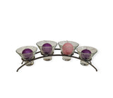 This elegant Danish Iron Arched Candle Holder for 4 candles includes three deep purple and one soft pink candle displayed in a set of glass holders on a sleek, curved metal stand.