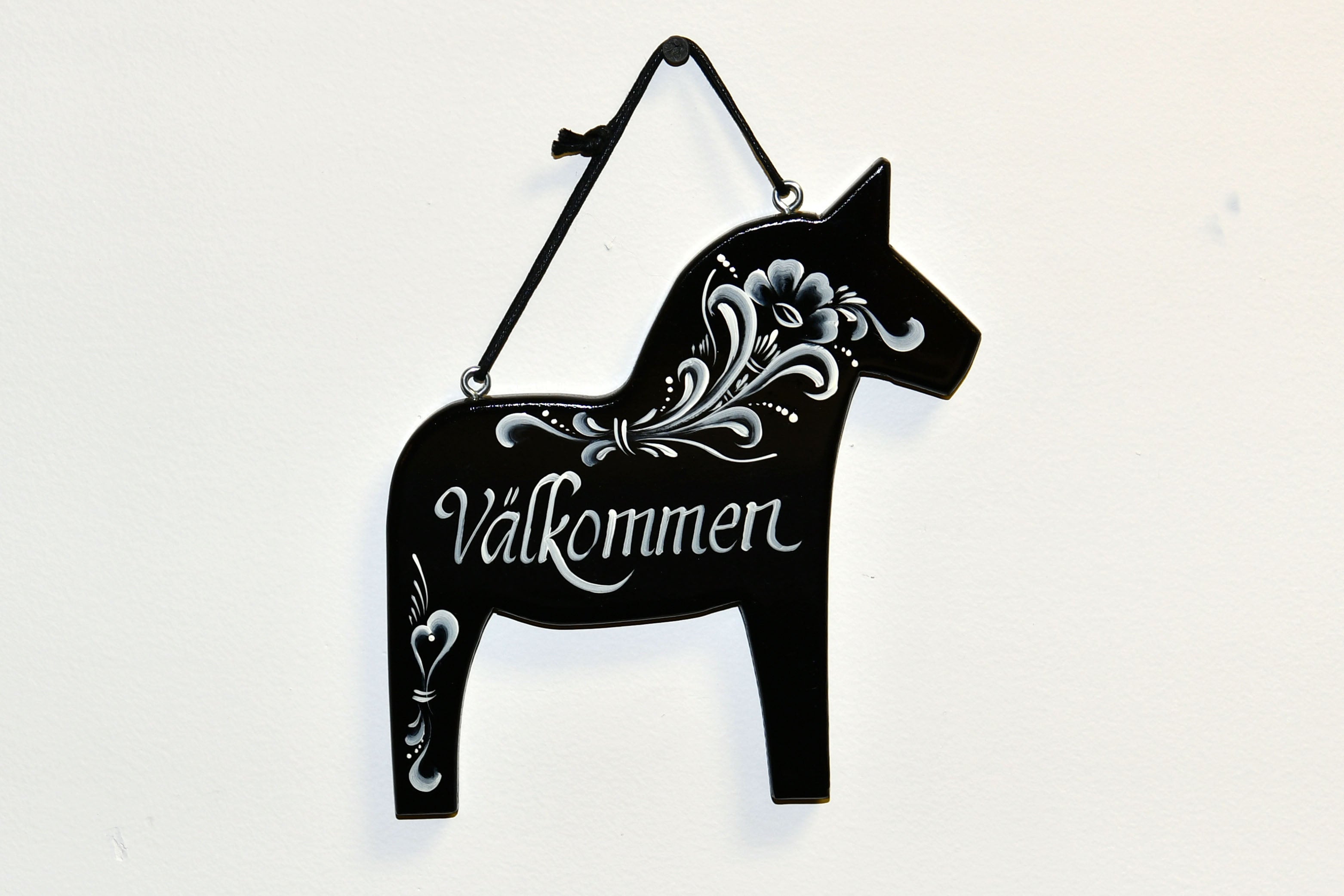 The Välkommen Welcome in Swedish Black Dala Horse Wall Decor is a charming horse-shaped sign featuring intricate white floral patterns and the word Välkommen, embodying Swedish hospitality.