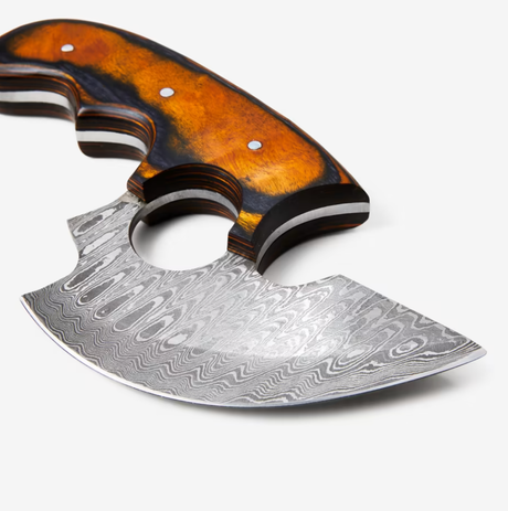 A close-up of the Knife: Alaskan Ulu Style Blade, featuring a curved High Carbon Damascus Steel blade with patterns and a polished brown wooden handle with finger grooves.