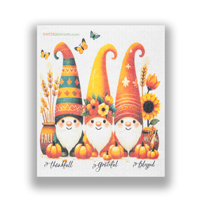 Reusable dish towel featuring three autumn gnomes surrounded by pumpkins, sunflowers, and butterflies against a background of vivid fall colors.