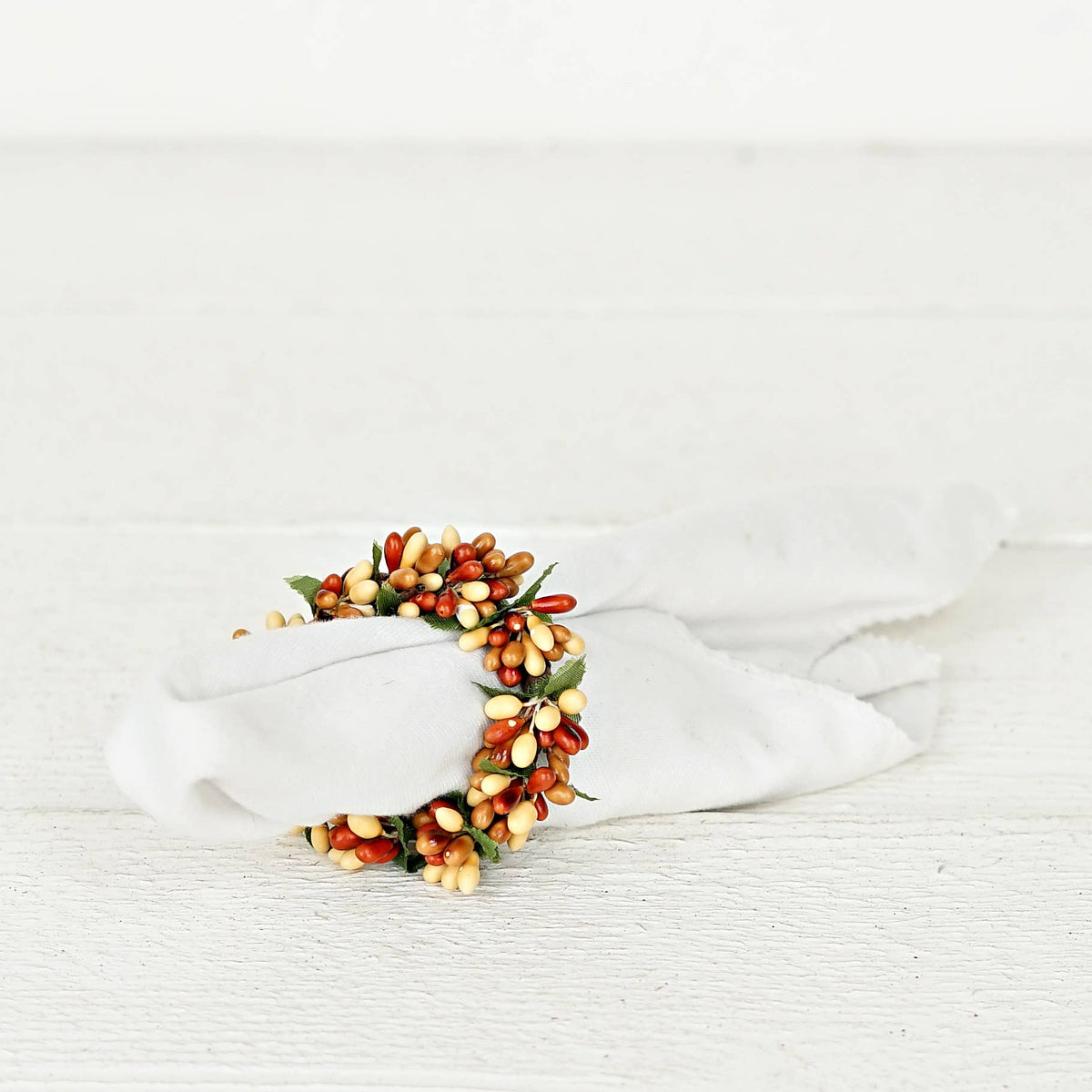 White cloth napkin secured in a napkin ring featuring faux autumn berries and green leaves.