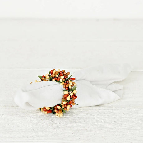 White cloth napkin secured in a napkin ring featuring faux autumn berries and green leaves.
