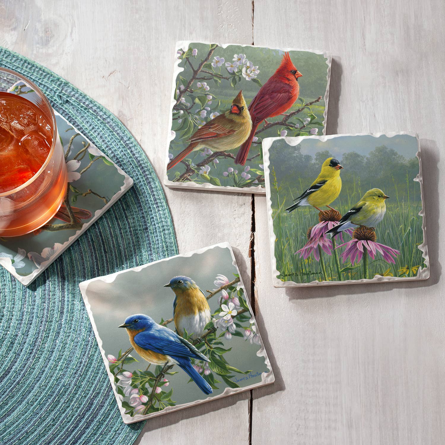 A drink with ice rests on one of the Beautiful Songbirds Assorted Image Tumbled Tile Coasters from the 4-pack placed on a light wooden table, highlighting both form and function.