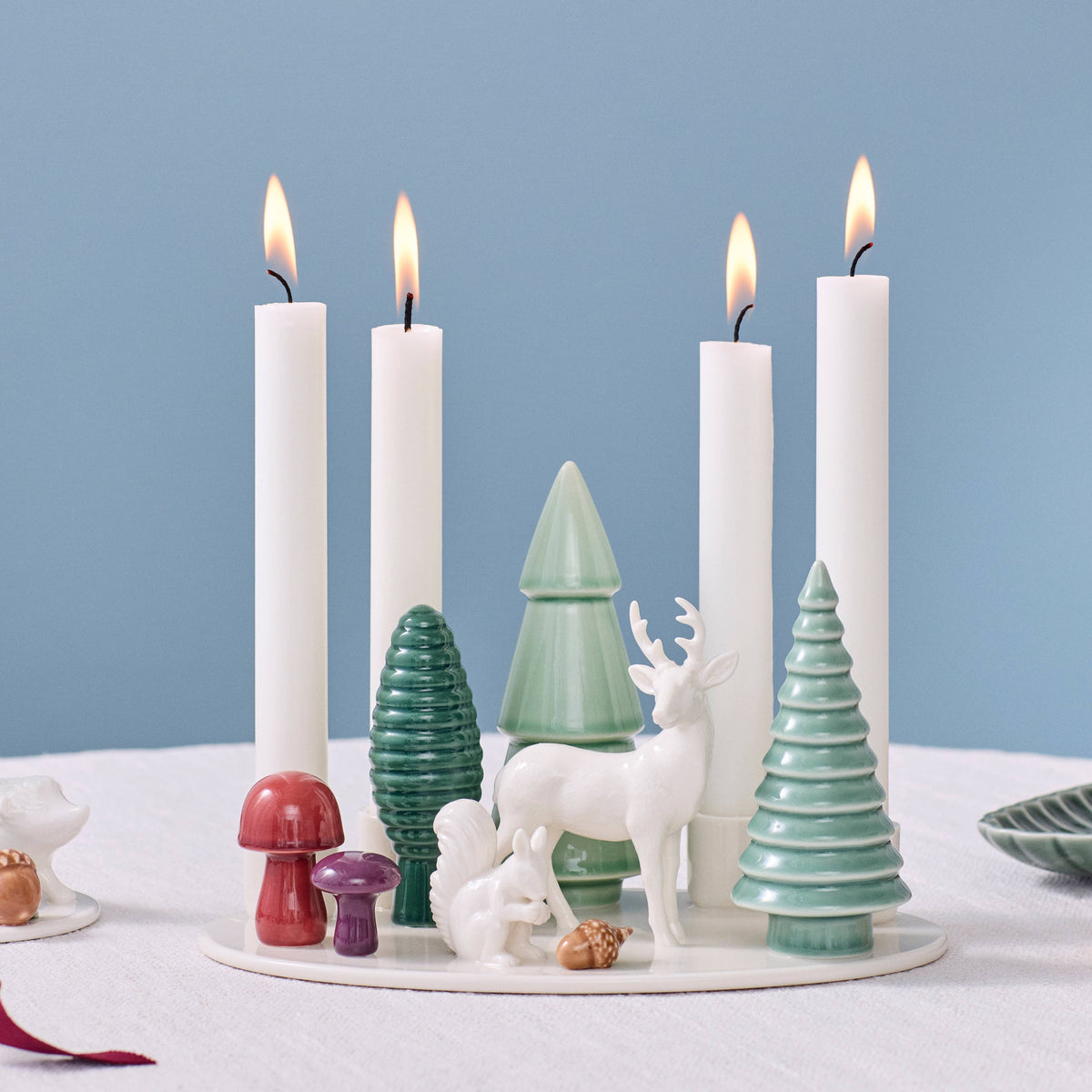 Handmade porcelain advent candle holder with four white candles, decorated with ceramic trees, a deer, a squirrel, and mushrooms.