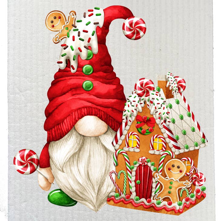 A dish cloth features a Christmas gnome sporting a red hat beside a gingerbread house adorned with candy canes and icing, topped with gingerbread cookies on both the house and the hat, embodying an eco-friendly scene akin to a biodegradable wonderland.