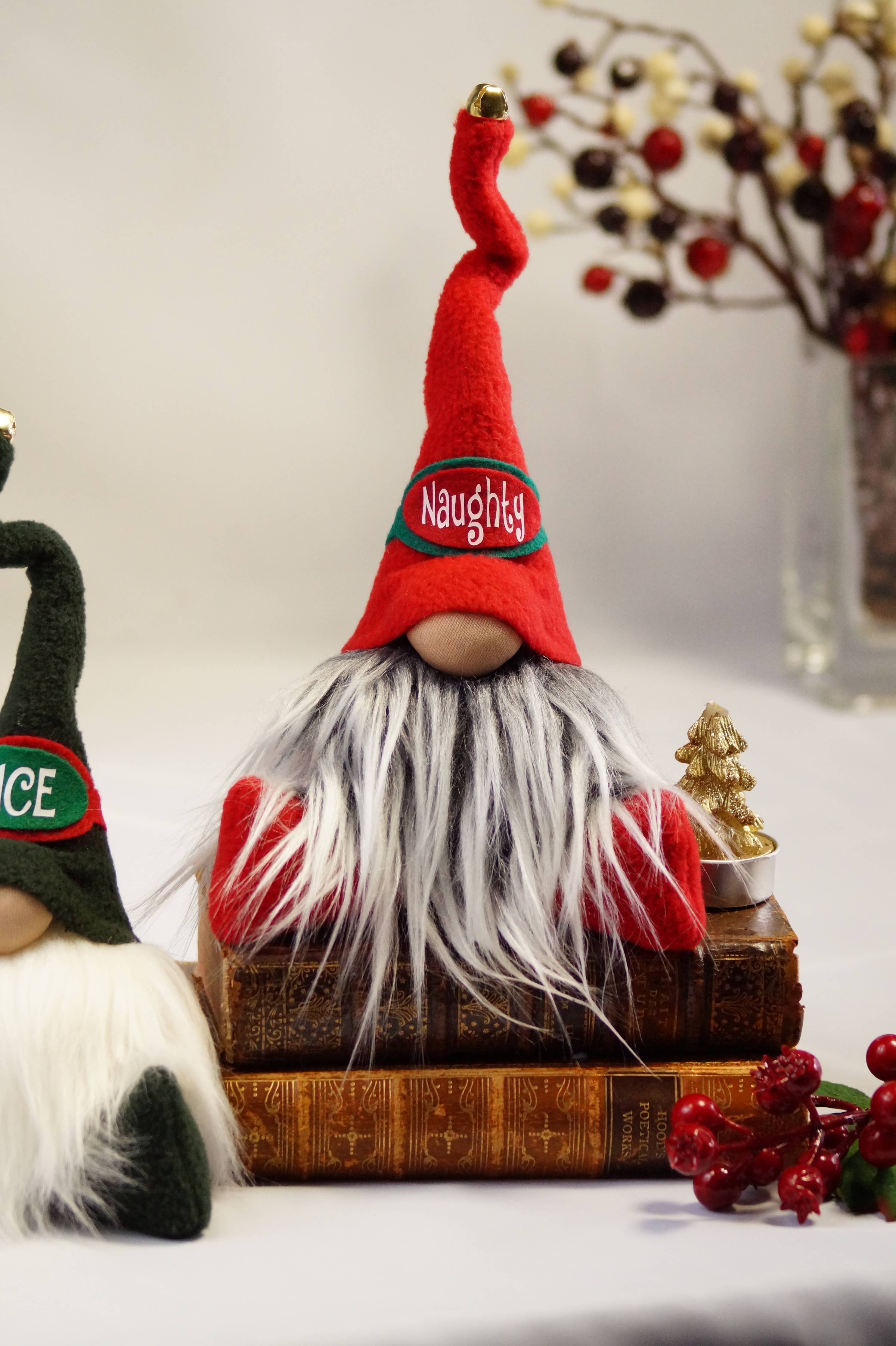 A Gnome: Naughty Christmas Gnome, featuring a handmade fleece hat, lounges on stacked books surrounded by red berries and blurred holiday decor.