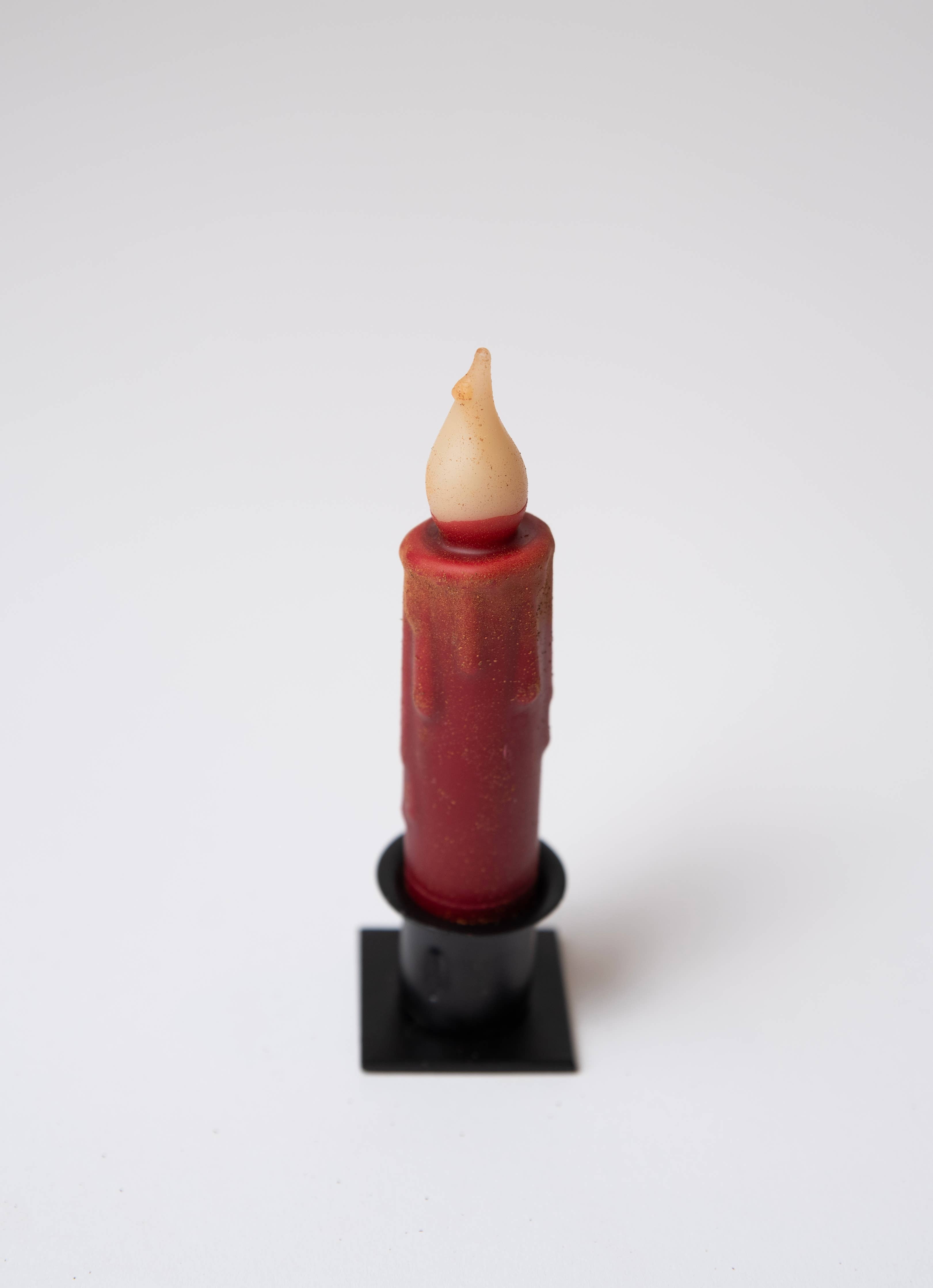 A Candle: Burgundy Cinnamon Dusted LED Timer Taper Candle: 7" sits upright in a black holder with a beige faux flame, battery operated, against a plain white background.