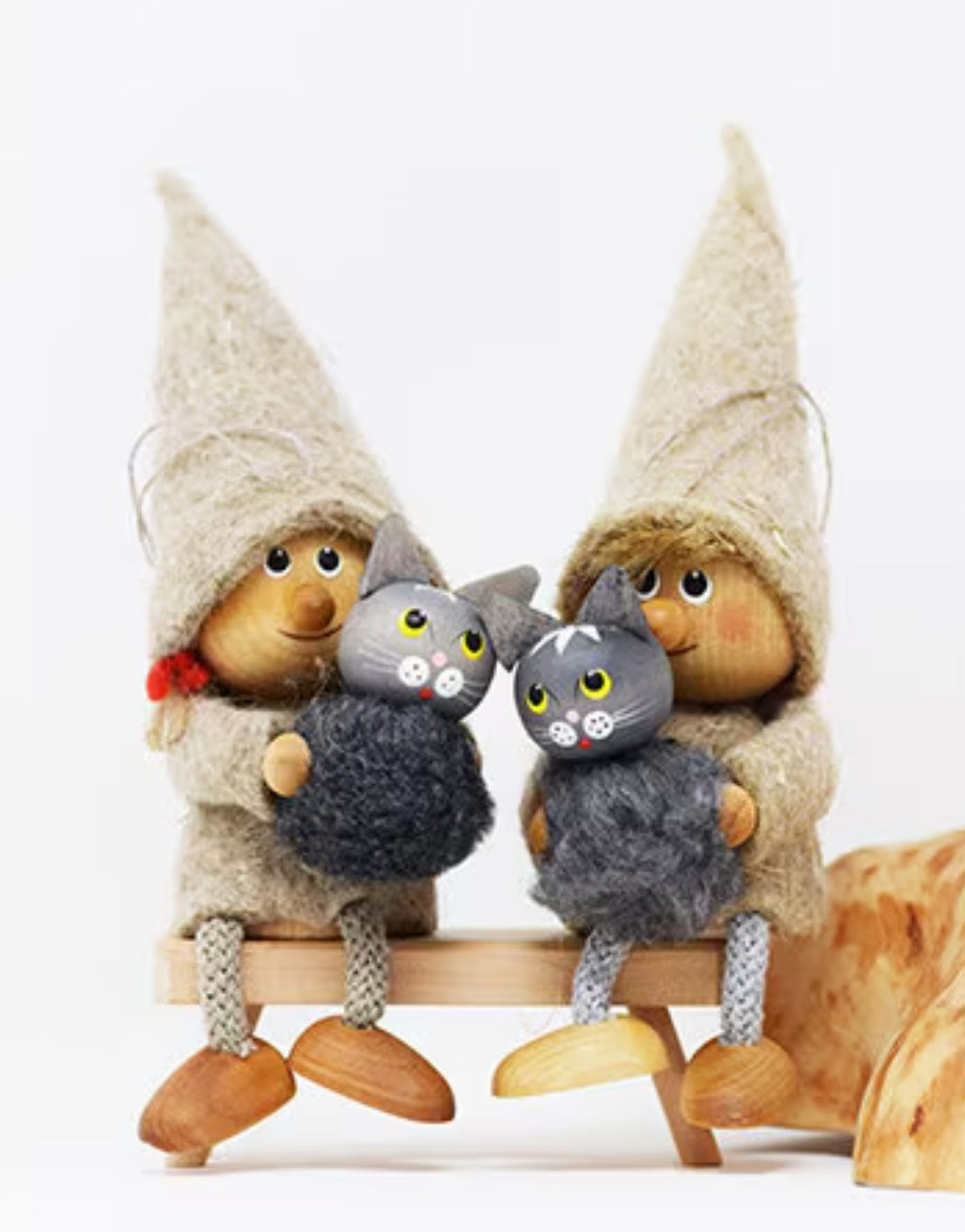 A 5" tall Girl Gnome figurine in a beige hat and coat sits on a shelf or hangs from a tree, holding a gray cat.