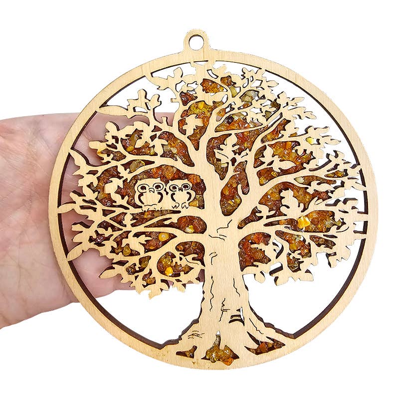 Hand holding the Ornament: Tree of Life with Two Owls Amber Suncatcher, a magnet featuring owls in a wooden tree, casting golden hues like an amber suncatcher.