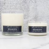 Two white soy wax candles in glass jars labeled “Fjord & Fable Candle: Kraken - Amber, Sea Salt, Driftwood & Leather 8oz,” set on white marble with a gray backdrop—perfect for adding bold amber and sea salt scent to any space.