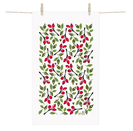 The Rose Hip Terry cotton towel by Anneko Design Sweden, featuring a classic Swedish pattern of green leaves, red berries, and black branches, hangs on a clothesline with two clothespins.
