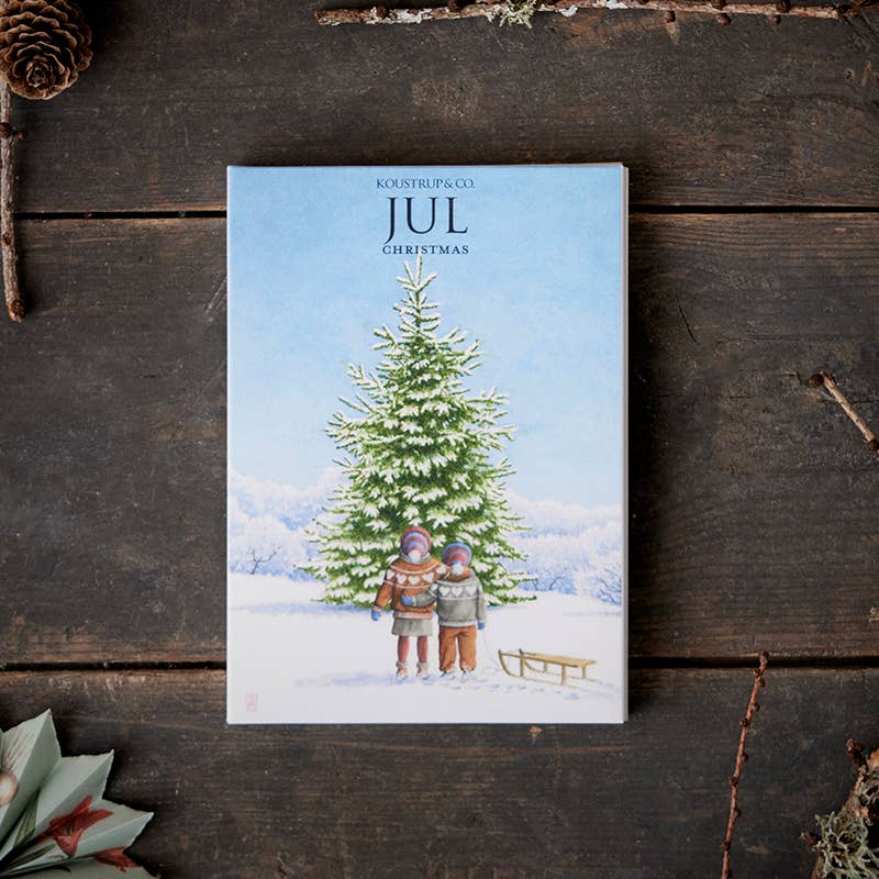 The card pack "Jul (Christmas)" from Koustrup & Co. features illustrations by Peter Nielsen, depicting two children in winter clothes standing by a Christmas tree in the snow, accompanied by a sled and forest gnomes peeking out from behind. The text on these charming cards reads "Jul Christmas," and each pack includes 8 cards with envelopes.