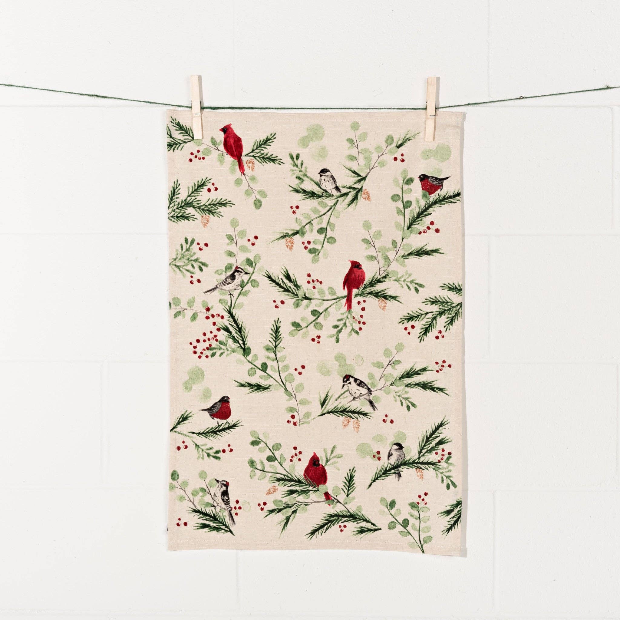 The Tea Towel: Forest Birds Christmas Dishtowel is displayed on a line, highlighting a design featuring birds perched on branches with green leaves and red berries, bringing a charming country atmosphere.