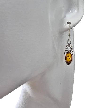 A mannequin displays Celtic dangle earrings crafted in sterling silver, each set with an oval cognac amber stone, highlighting the unique charm of the Earrings: Celtic Dangle Cognac Amber Sterling Silver Earrings.