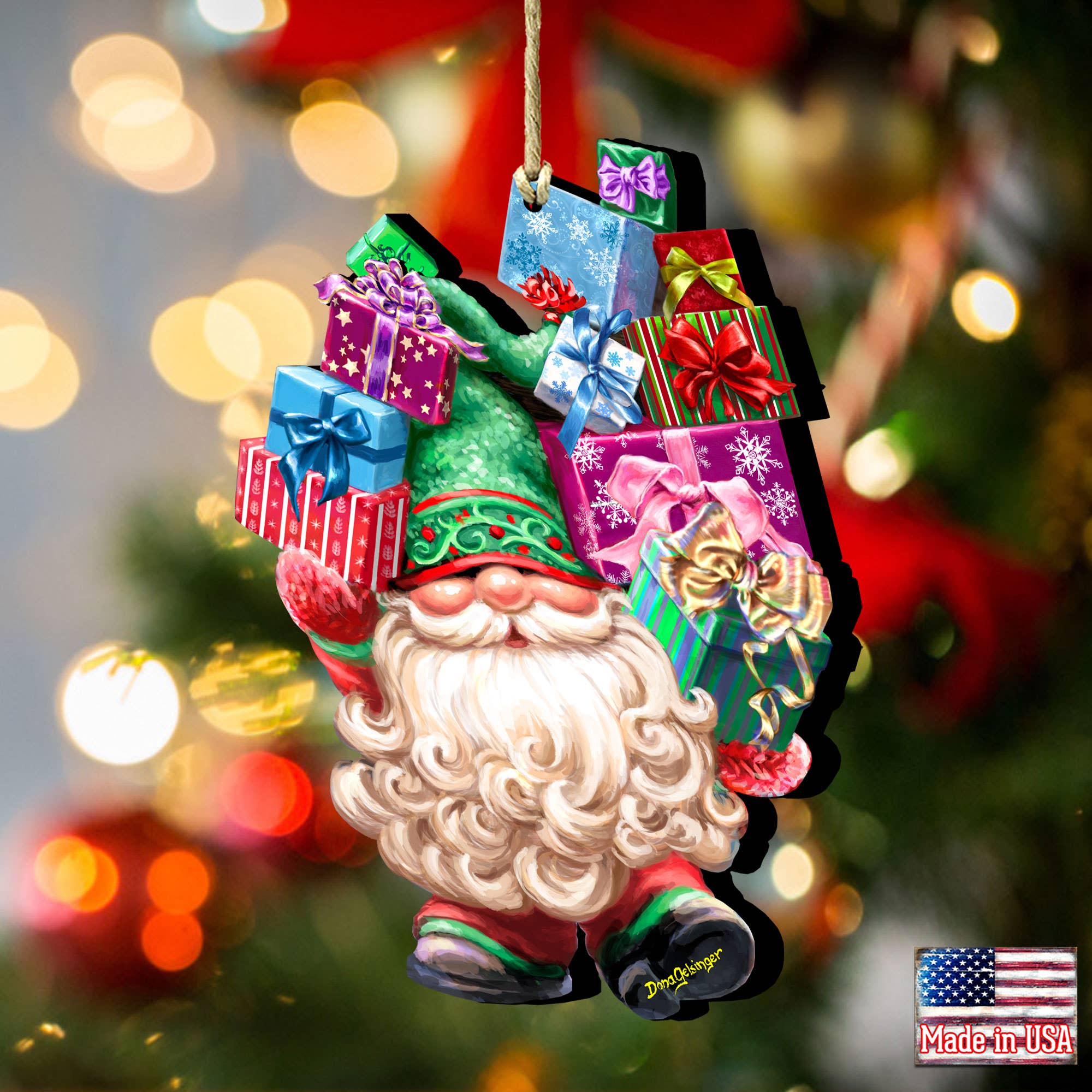 The Gift Giver Gnome Handcrafted Ornament by D.Gelsinger features a unique festive style as it presents colorful gift boxes, set against a backdrop of blurred Christmas lights. A "Made in USA" label is prominently displayed in the corner of the image.