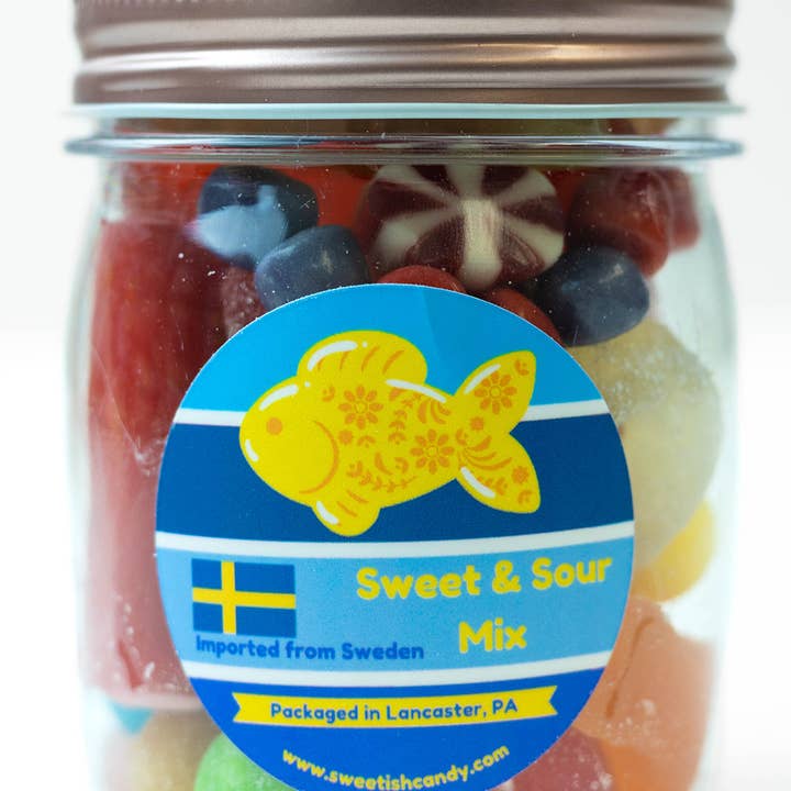 The beautifully packaged clear jar of Sweetish Sweet & Sour Mix candy, featuring a rose gold lid and a fish graphic, holds an 8oz assortment of colorful treats. Imported from Sweden and packaged in Lancaster, PA.