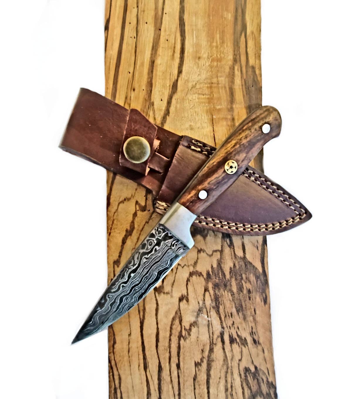 The Knife: Cheff - Damascus Paring Knife features a handcrafted Damascus steel blade and wooden handle, resting on a brown leather sheath atop a wooden surface.
