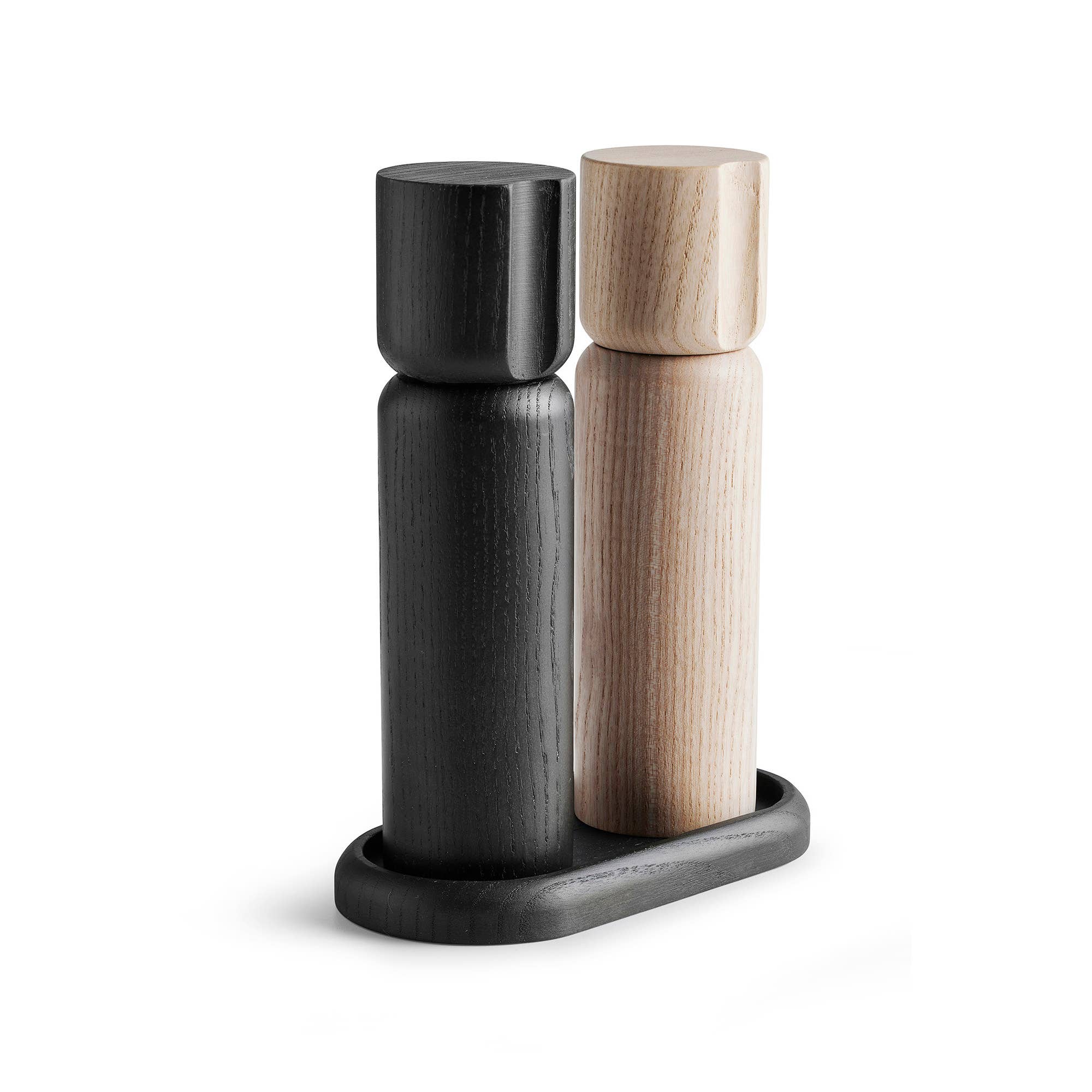 The Shakers Salt and Pepper Grinder Set from Sweden, featuring durable ceramic grinders, includes two elegant wooden grinders—one black, the other ash wood—standing on a small oval tray.