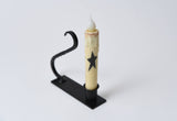 Battery-operated taper candle with a black star design in a black iron holder with a curved handle.