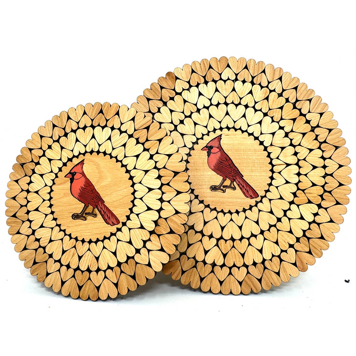 The handmade Trivet: Red Cardinal Wooden Trivet with Laser Cut Hearts features a circular wooden design, decorated with heart-shaped patterns and a central red cardinal illustration, crafted in Estonia.