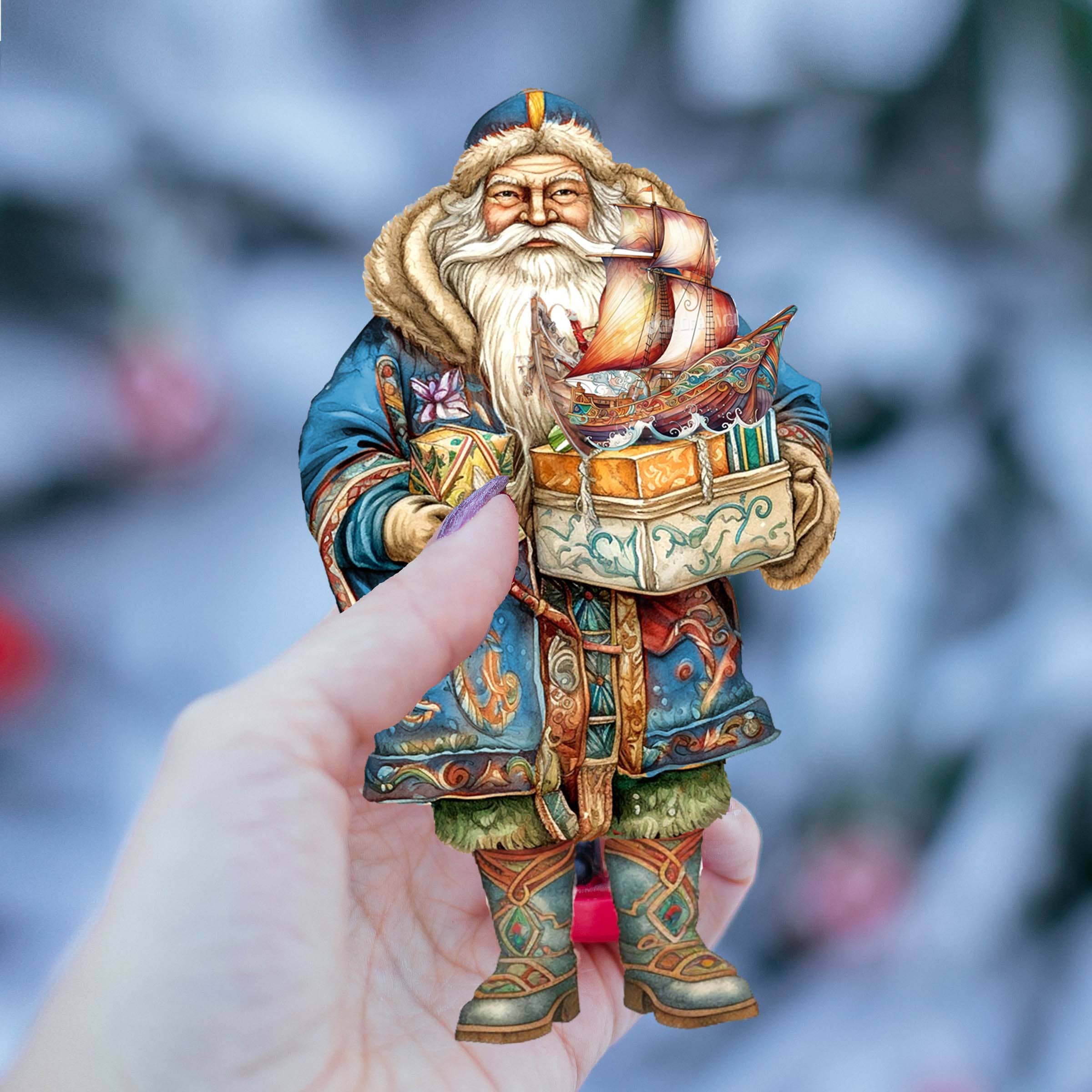 Hand holding an intricately carved Nordic-inspired Santa Claus figurine, adorned with an ornate blue coat and holding a model ship. This piece is part of the exquisite handcrafted keepsake collection by G.DeBrekht art studio, known as the "Ornament: Nordic Santa - Wooden Ornament.