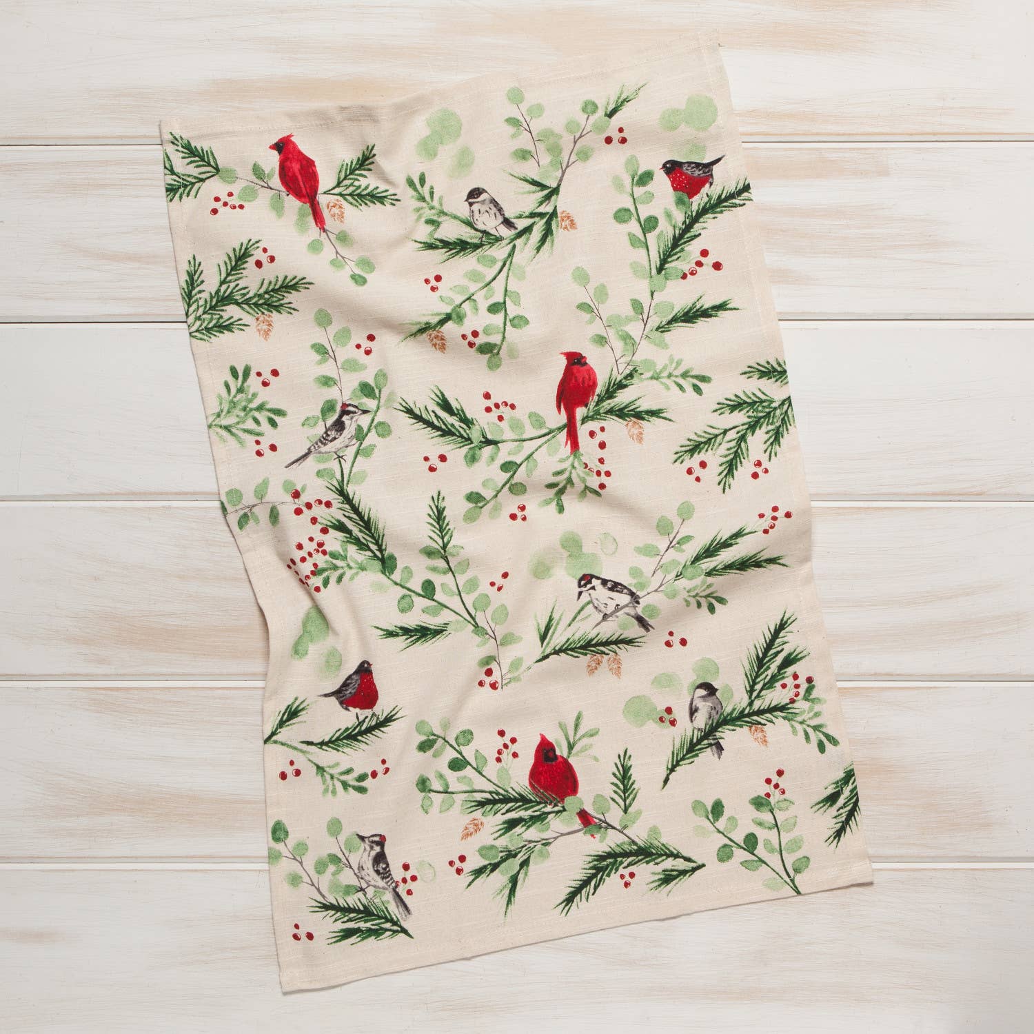 The "Forest Birds Christmas Dishtowel" tea towel, adorned with a pattern of red and gray forest birds perched on branches among green leaves and red berries against a light wooden background, brings about a delightful country ambiance.