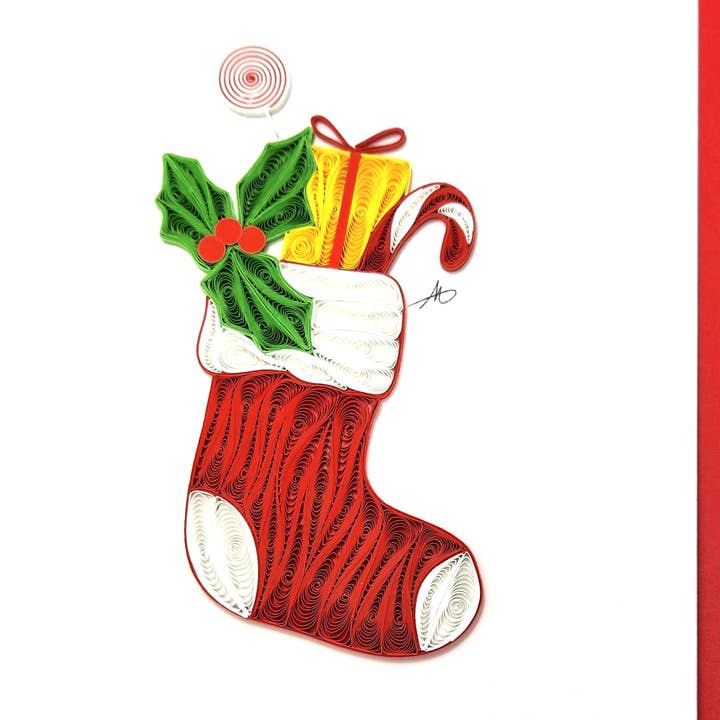 The Cards: Christmas Stocking Quilling Card is an exquisite hand-crafted piece showcasing a charming red Christmas stocking filled with festive treats such as a candy cane, yellow gift, green holly leaves, and a peppermint swirl.