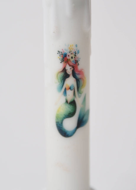 The Candle: Mermaid LED Timer Taper Candle features a vibrant mermaid with rainbow hair and a floral crown, bringing whimsical charm to any space.