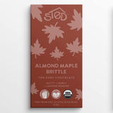 Rust-colored chocolate bar wrapper with pink maple leaf pattern, text indicating almond maple brittle and 70% dark chocolate, organic and allergy-friendly icons visible.