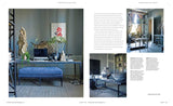 A Scandinavian-style home office featuring blue walls, wooden floors, a velvet bench, desk, sculptures, plants, framed art, and the book New Nordic Colour by Antonia af Petersens.