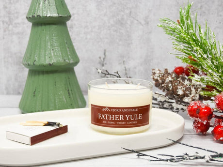 The Candle: Father Yule Premium Soy Candle by Fjord & Fable (4oz jar, 2 wicks, 20+ hour burn) sits on a tray with a matchbox and festive decor—ideal for bringing a warm Yuletide scent to your holiday gatherings.
