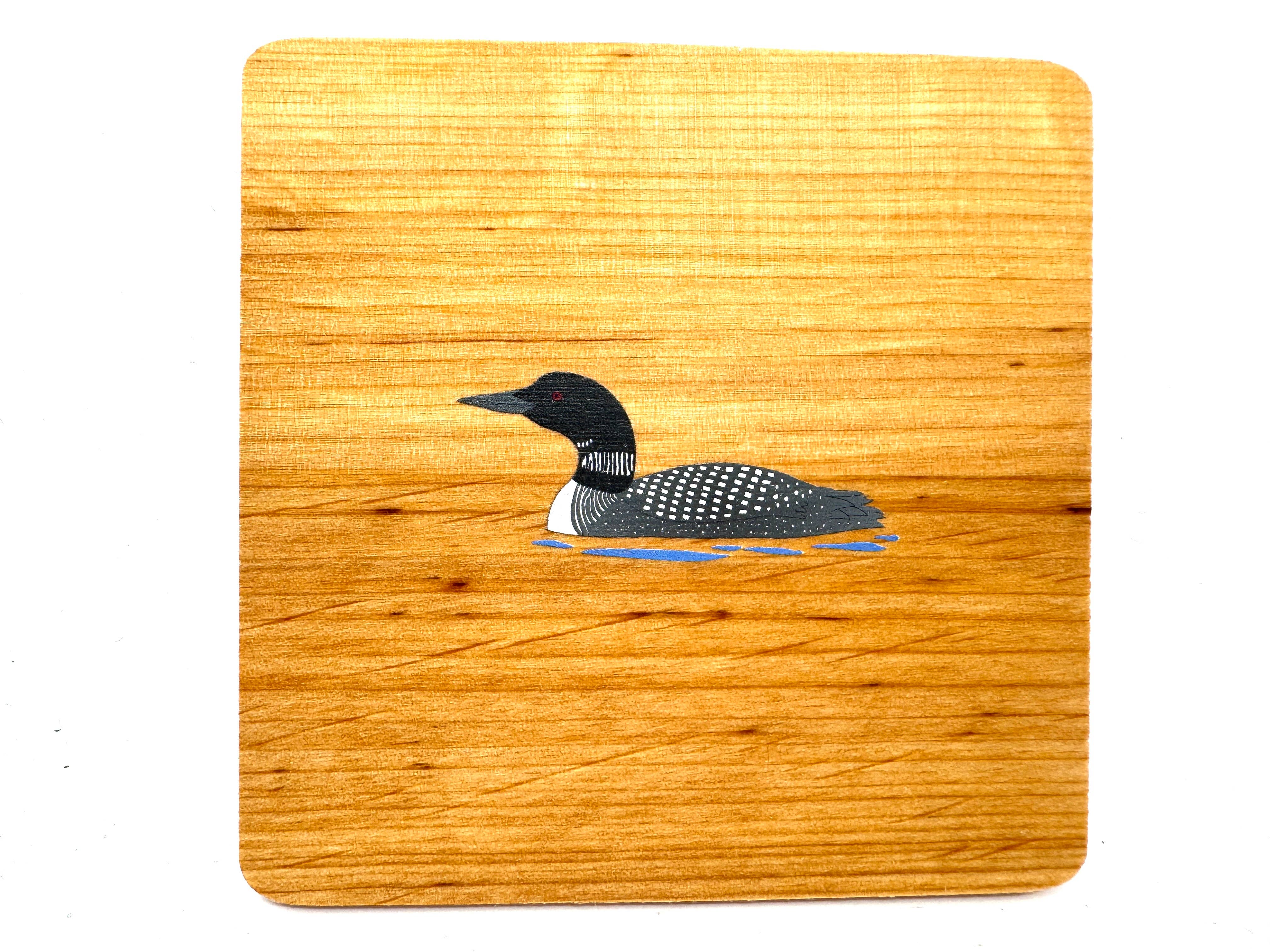 Introducing the "Coaster: Alder Wood Coaster with Loon," a beautifully crafted piece featuring a captivating loon gracefully gliding across serene waters, all handmade from alder wood.