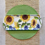 The Tray: Sunflower & Bluebonnets Floral Loaf Serving Charcuterie Tray, with charming sunflower and bluebonnet designs, sits on a green woven placemat atop a beige runner. This eco-friendly bamboo tray adds elegance to any table setting.