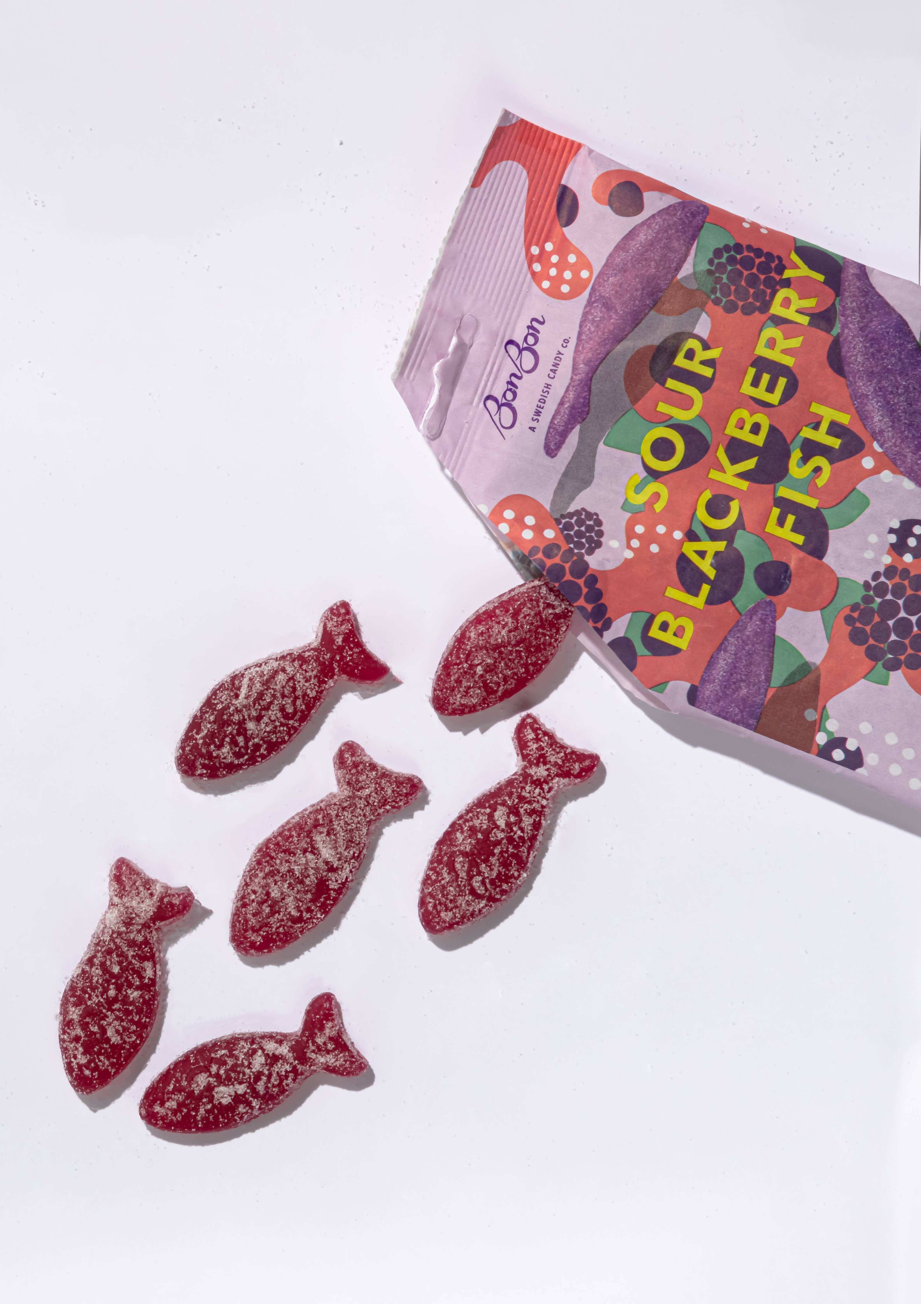 A partially opened bag of Bon Bon Sour Blackberry Fish candy with six fish-shaped gummies scattered outside.