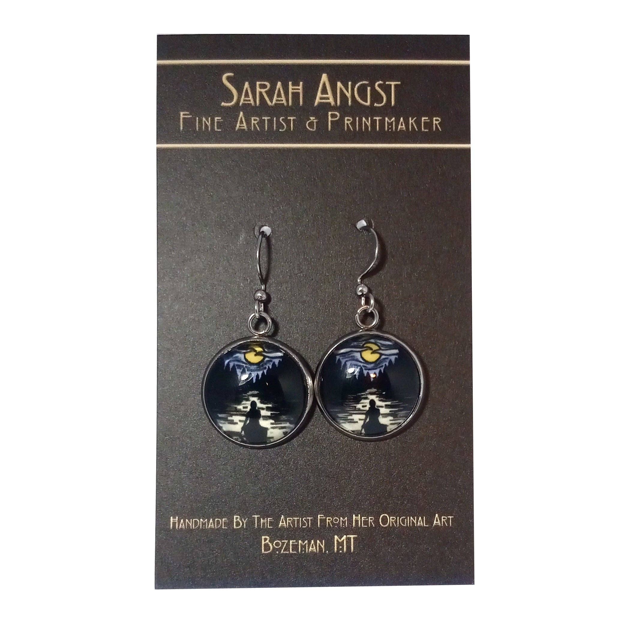 These handcrafted earrings, labeled as "Solitude Canoe" by Sarah Angst, elegantly display a night sky and mountain design on a card marked with the branding of Sarah Angst Art, Fine Artist & Printmaker.