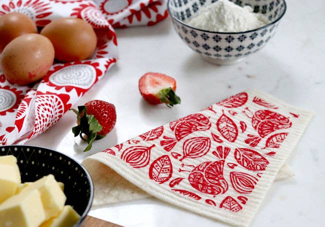 Ingredients for baking on a countertop: eggs, strawberries, a bowl of flour, and a bowl of butter rest upon Scandinavian-style, Robins - Red dish cloths made from all-natural materials.