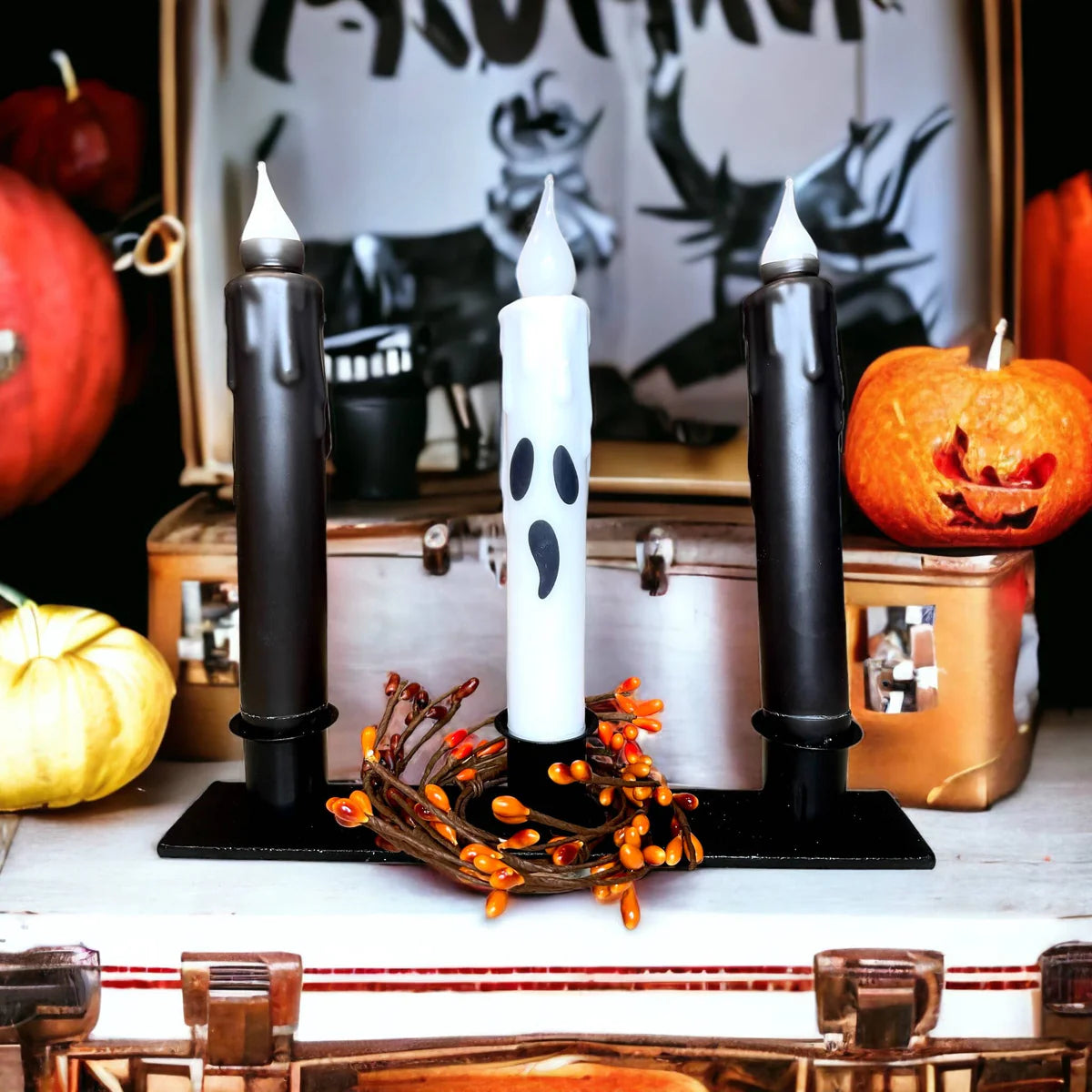 A farmhouse décor charm is evoked with three candles on a stand, featuring two black hand-dipped beeswax tapered LED light candles and a white ghost-themed one at the center, surrounded by pumpkins and a Halloween sign for an inviting seasonal touch.