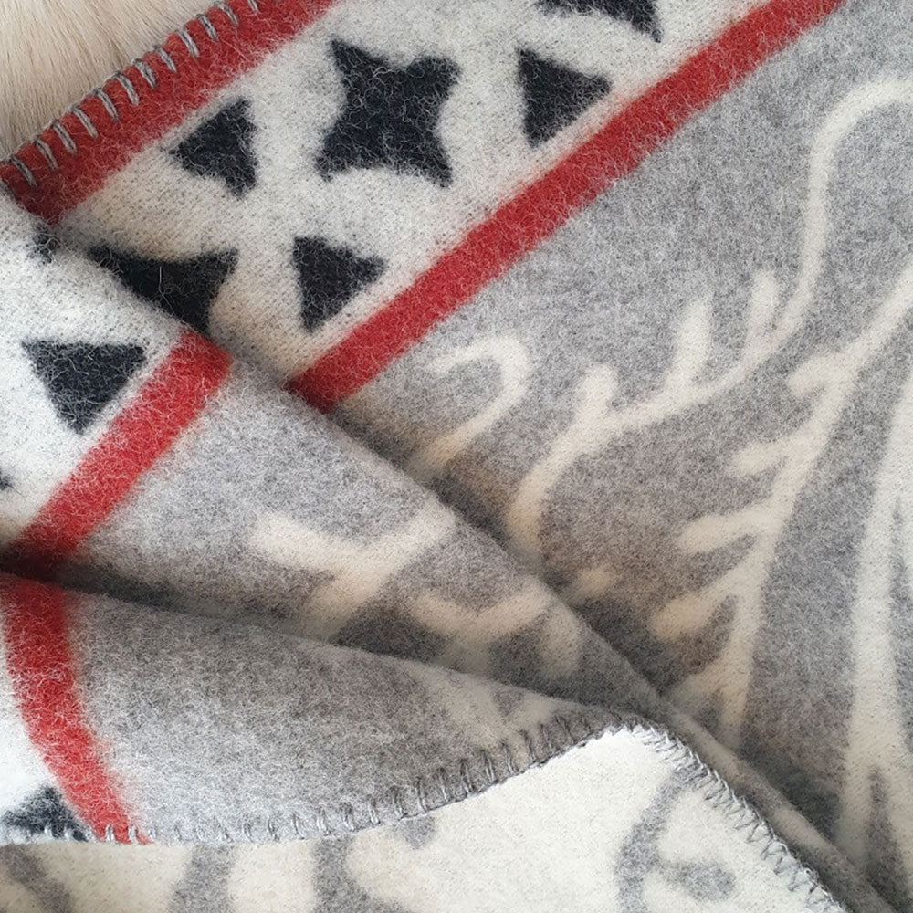 Close-up of the Albertus blanket by Kerstin Landstrom, made from 100% Norwegian lambswool, showcasing a red stripe and black star pattern with an intricate white design.