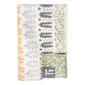 Folded wool blanket with yellow, gray, and green leaf patterns on white; a corner is turned to show the reverse side. Scandinavian design by Kerstin Landström.