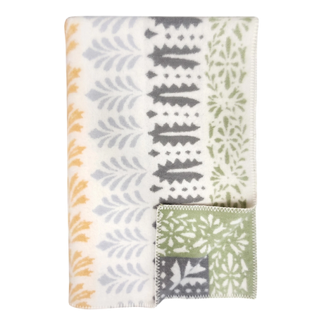 Folded wool blanket with yellow, gray, and green leaf patterns on white; a corner is turned to show the reverse side. Scandinavian design by Kerstin Landström.
