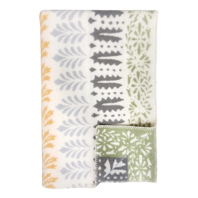 Folded wool blanket with yellow, gray, and green leaf patterns on white; a corner is turned to show the reverse side. Scandinavian design by Kerstin Landström.