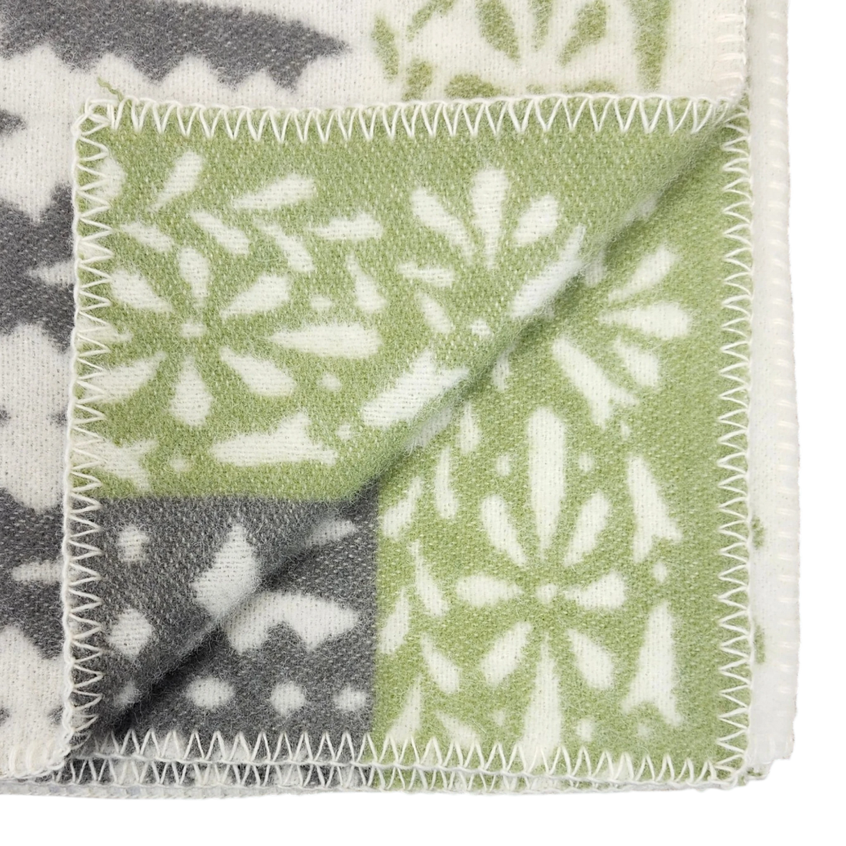 Close-up of a folded wool blanket corner featuring green, gray, and white snowflake patterns with zigzag stitched edges.