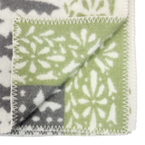 Close-up of a folded wool blanket corner featuring green, gray, and white snowflake patterns with zigzag stitched edges.
