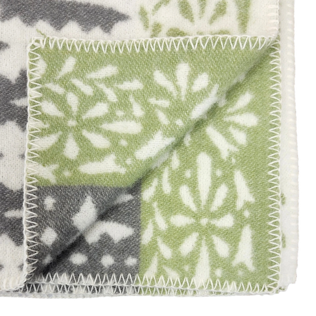 Close-up of a folded wool blanket corner featuring green, gray, and white snowflake patterns with zigzag stitched edges.