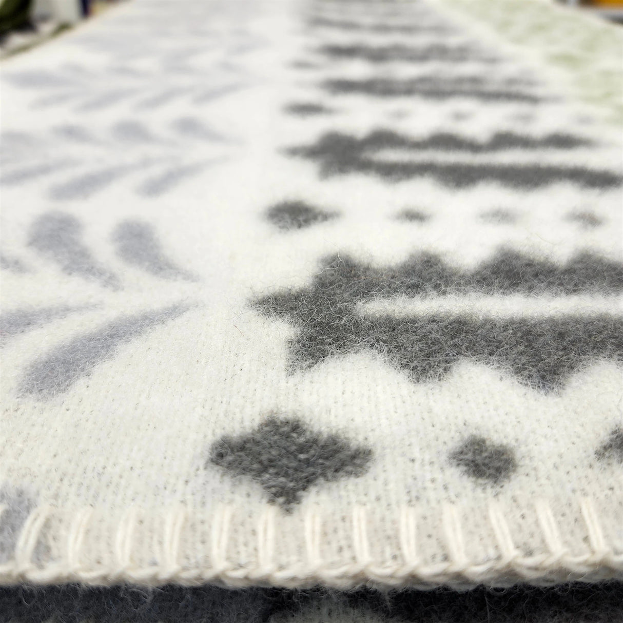 Close-up of a Swedish design blanket featuring a white base with gray geometric and tree-like patterns. The material texture is clearly visible.