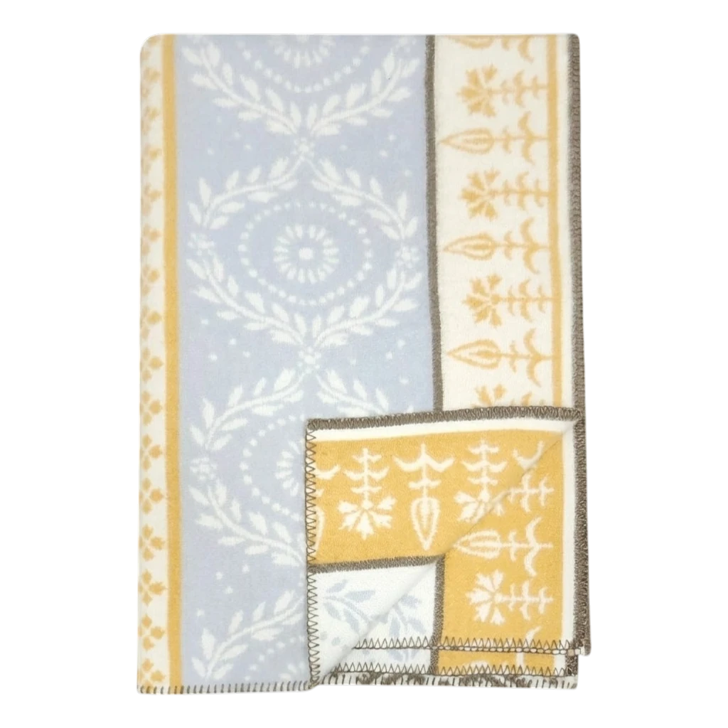 Folded lambswool blanket featuring blue and yellow sections, white floral and geometric patterns, and brown stitched edges.