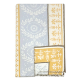 Folded lambswool blanket featuring blue and yellow sections, white floral and geometric patterns, and brown stitched edges.