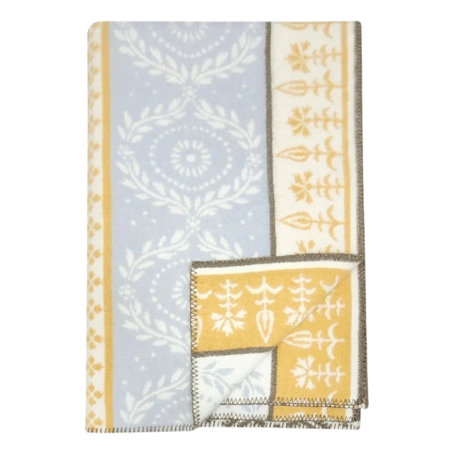 Folded lambswool blanket featuring blue and yellow sections, white floral and geometric patterns, and brown stitched edges.