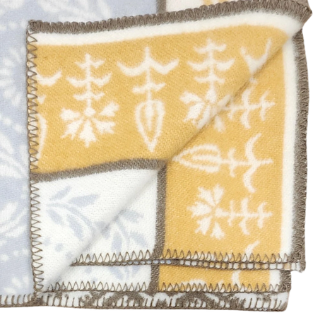 Folded Swedish wool blanket with a yellow and white botanical pattern on one side, pale blue reverse, and dark stitched edges.